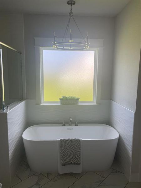 Bathroom with a chandelier, marble look tile flooring, a freestanding bath, tile walls, and a wainscoted wall Bathroom with a chandelier, marble look tile flooring, a freestanding bath, tile walls, and a wainscoted wall