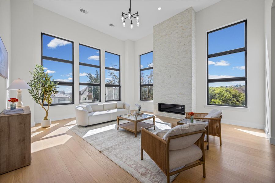 Living area with a high ceiling, light wood-style floors, a stone fireplace, and hanging lights