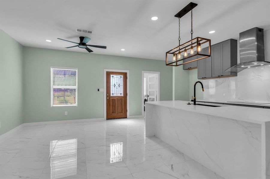 Kitchen featuring wall chimney range hood, light marble finish flooring, recessed lighting, light stone counters, and hanging light fixtures Kitchen featuring wall chimney range hood, light marble finish flooring, recessed lighting, light stone counters, and hanging light fixtures