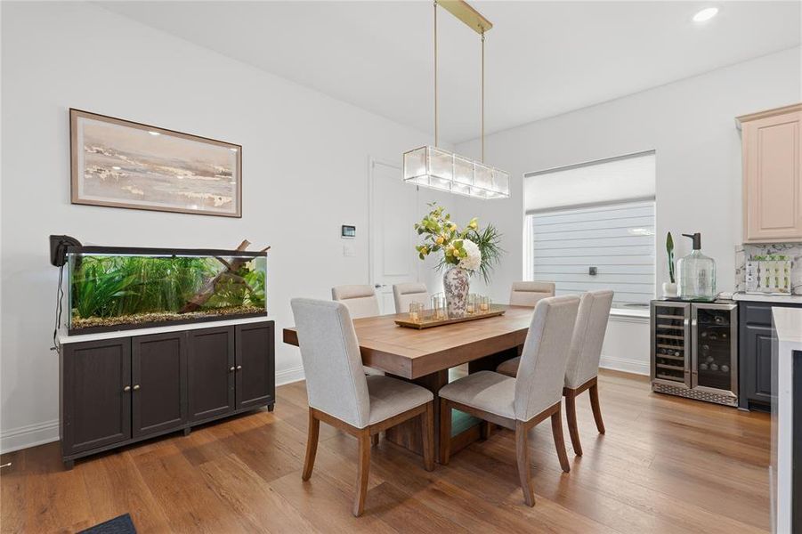 Dining area featuring wood-finish flooring, a contemporary linear chandelier, a large window with privacy blinds, and built-in cabinetry Dining area featuring wood-finish flooring, a contemporary linear chandelier, a large window with privacy blinds, and built-in cabinetry