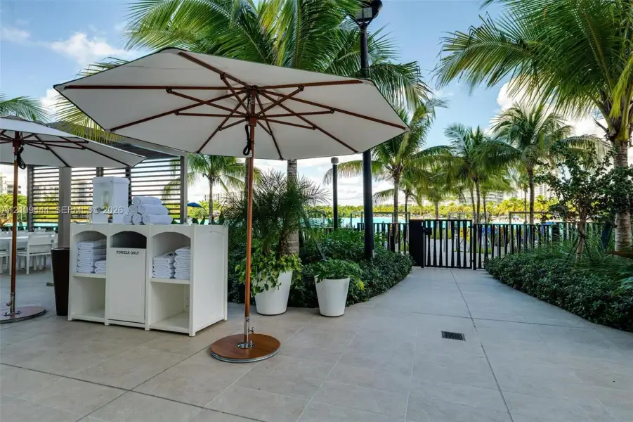 Outdoor terrace featuring large-format tile flooring, built-in towel storage console, mature palm trees, and metal fencing