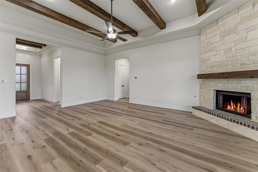 Expansive living area featuring wood-finish flooring, a tray ceiling with exposed wood beams, and a ceiling fan Expansive living area featuring wood-finish flooring, a tray ceiling with exposed wood beams, and a ceiling fan