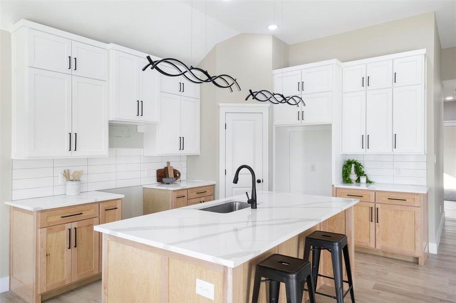 Kitchen featuring white cabinets, a center island with sink, sink, and backsplash