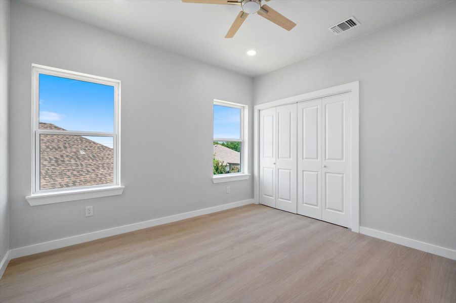 Natural light floods this inviting bedroom with light-toned hardwood flooring and a ceiling fan.