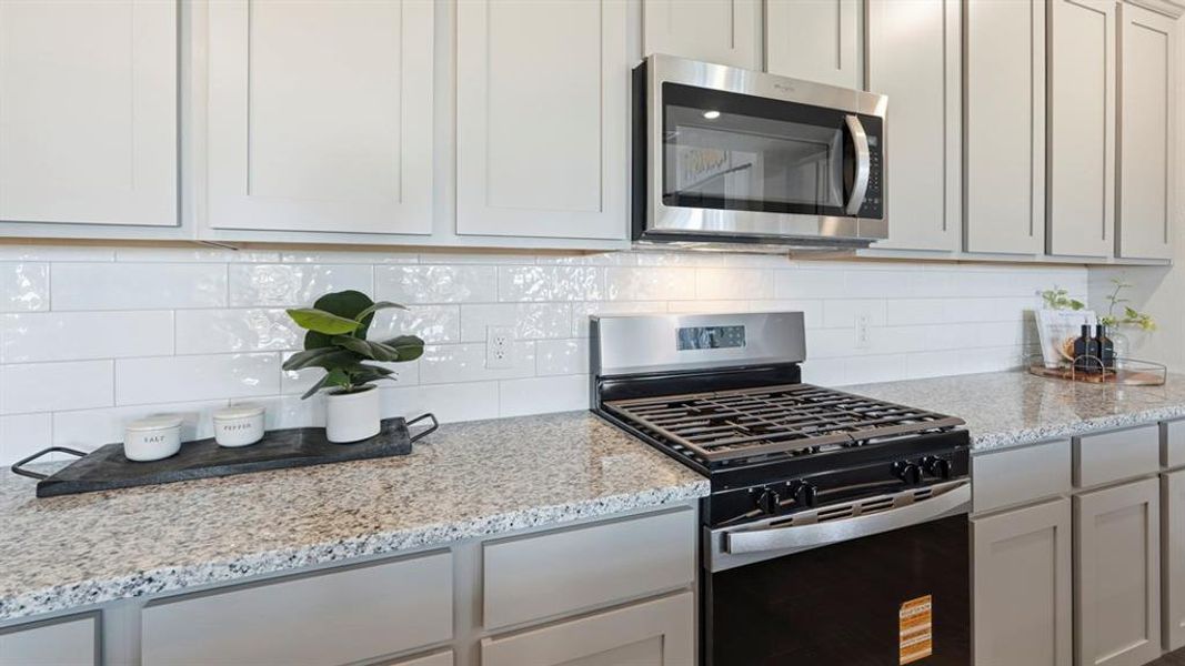 Kitchen featuring a gas range, stainless steel microwave, white subway tile backsplash, light-toned countertops, and shaker-style cabinetry Kitchen featuring a gas range, stainless steel microwave, white subway tile backsplash, light-toned countertops, and shaker-style cabinetry