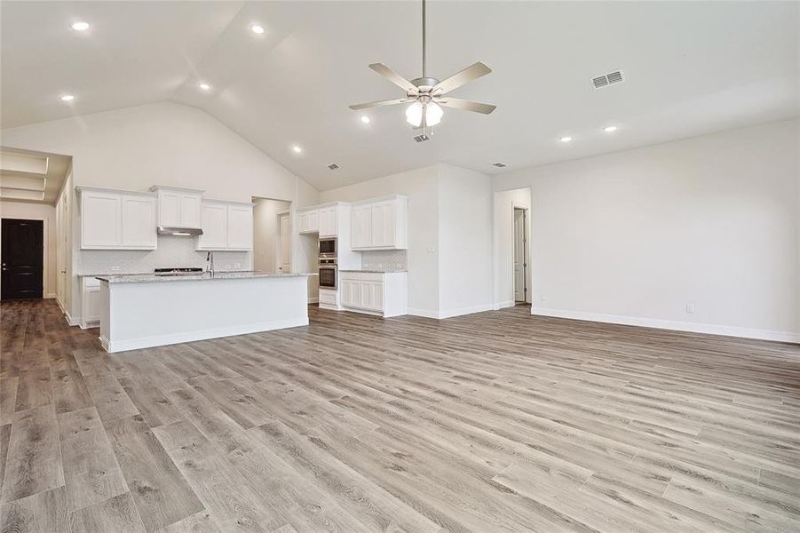 Unfurnished living room with ceiling fan, light wood-type flooring, and high vaulted ceiling