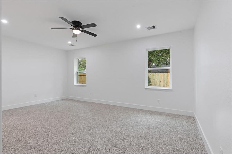 This is a bright, freshly painted room with two windows providing natural light, a modern ceiling fan, and new carpet flooring. The space is ready for personalization.