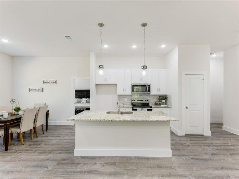 Kitchen featuring tasteful backsplash, a center island with sink, hanging light fixtures, appliances with stainless steel finishes, and white cabinets