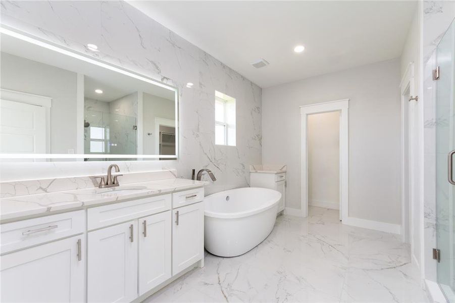 Bathroom with light marble finish floors, a marble finish shower, vanity, a freestanding bath, and recessed lighting