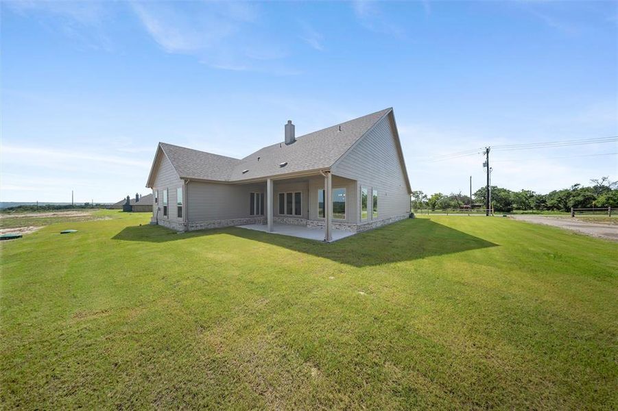 Rear view of house featuring a patio, a yard, roof with shingles, and stone siding Rear view of house featuring a patio, a yard, roof with shingles, and stone siding