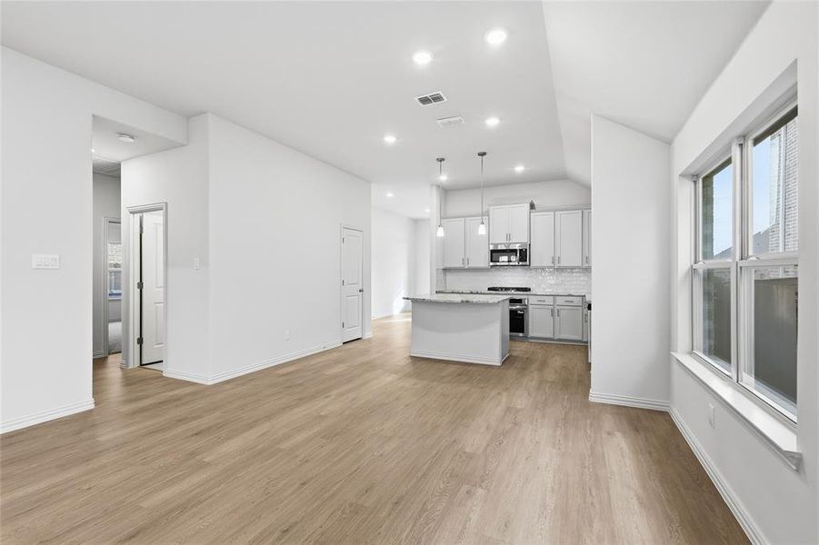 Kitchen with a kitchen island, hanging light fixtures, light wood-style flooring, tasteful backsplash, and stainless steel appliances Kitchen with a kitchen island, hanging light fixtures, light wood-style flooring, tasteful backsplash, and stainless steel appliances