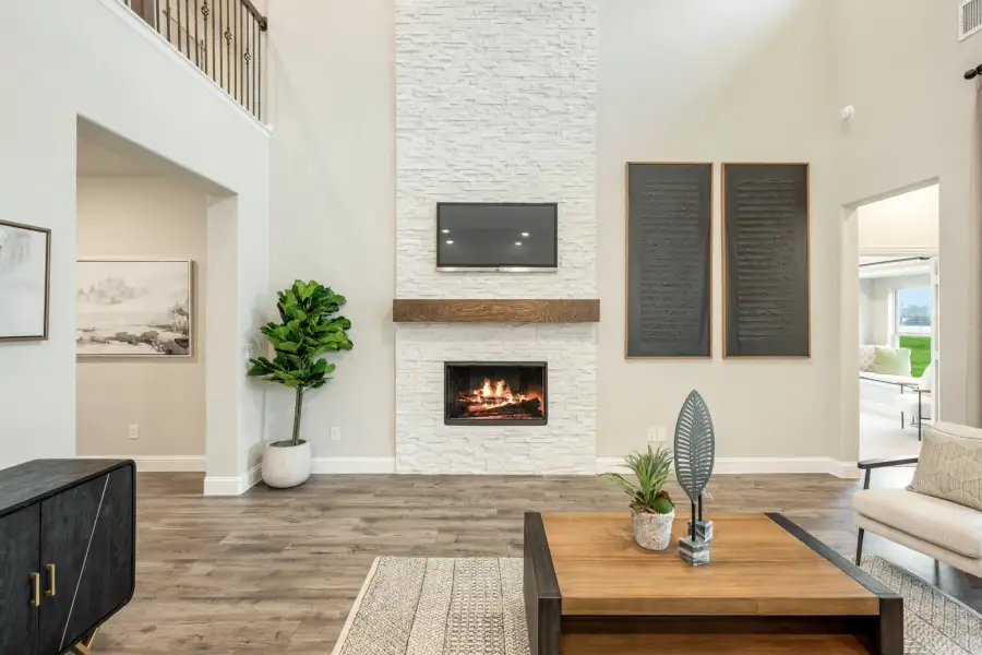 Living room with two-story white stone fireplace, wall-mounted TV, wood mantel, and hardwood floors