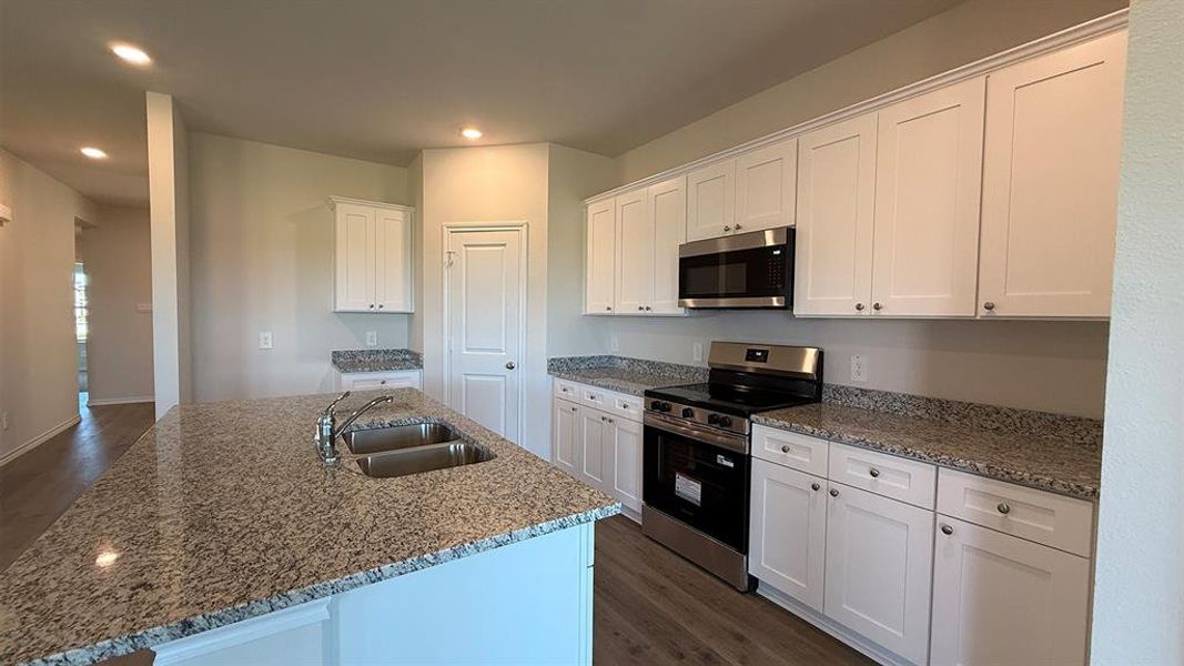 Kitchen featuring a large island with an undermount double-basin sink, granite countertops, white shaker-style cabinetry, and stainless steel appliances