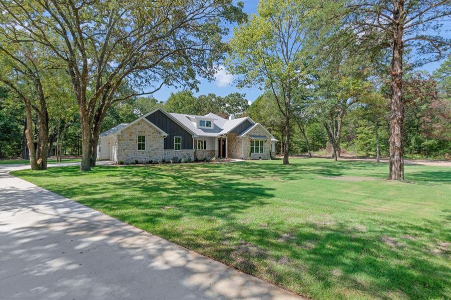 Craftsman house featuring a front lawn, stone siding, board and batten siding, and view of scattered trees Craftsman house featuring a front lawn, stone siding, board and batten siding, and view of scattered trees