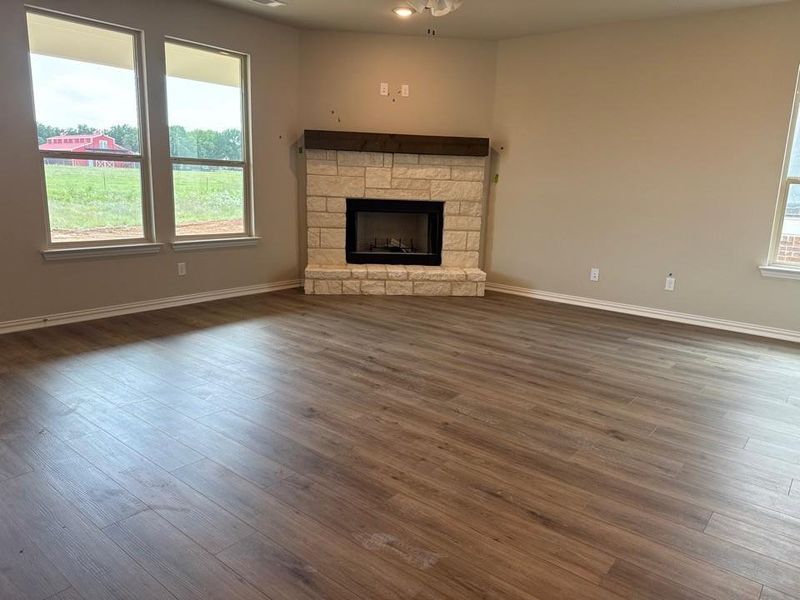 Spacious living area featuring wood-finish flooring, a stone-clad fireplace with a wood mantel, and multiple windows