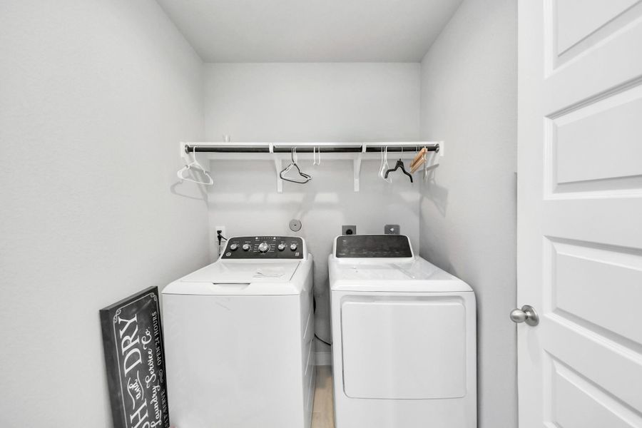 The laundry zone has ample elbow room, featuring built-in overhead storage with an integrated hanging bar to simplify chores.