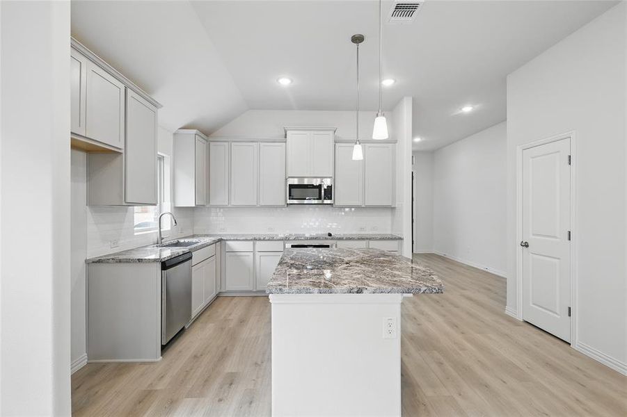 Kitchen with a center island, light stone countertops, stainless steel appliances, hanging light fixtures, and vaulted ceiling