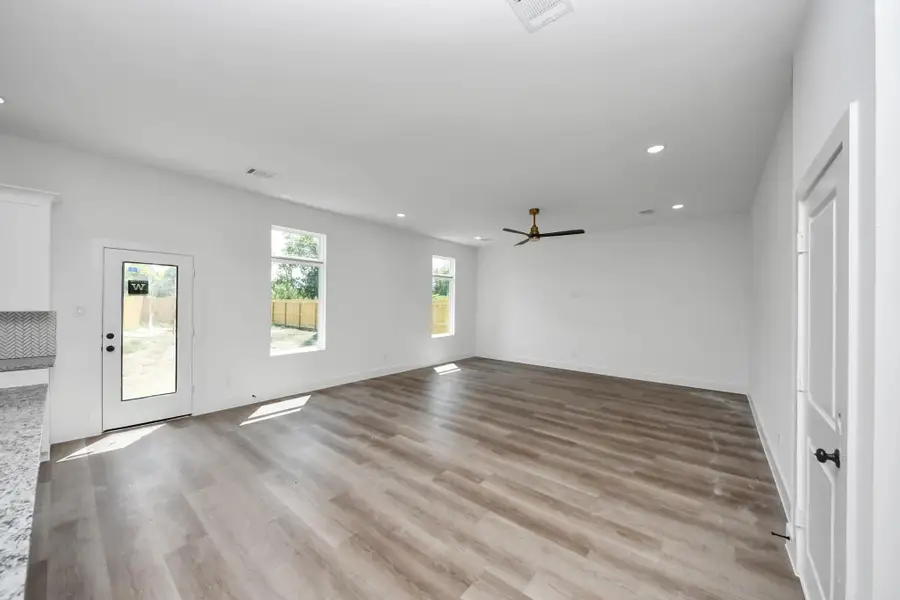 Living Room – Spacious living room featuring wood-look flooring, abundant natural light, recessed lighting, and a modern ceiling fan.