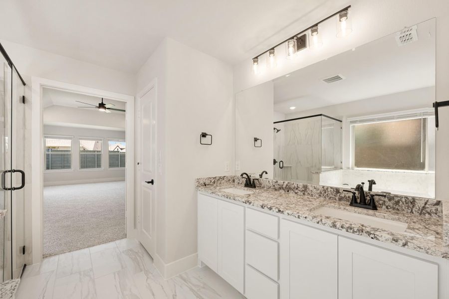 Ensuite bathroom with double vanity, granite countertops, white cabinets, and glass shower enclosure