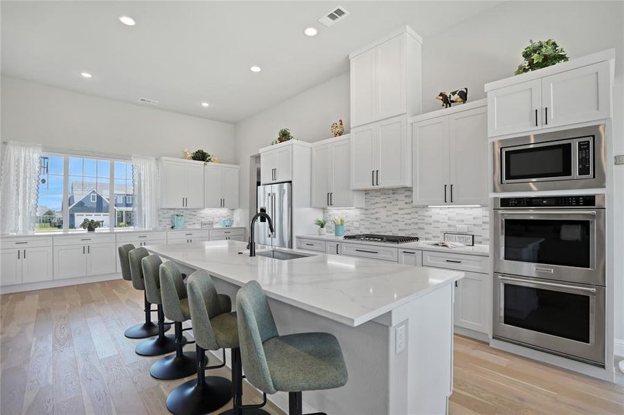 Kitchen featuring appliances with stainless steel finishes, a sink, a kitchen breakfast bar, decorative backsplash, and white cabinets Kitchen featuring appliances with stainless steel finishes, a sink, a kitchen breakfast bar, decorative backsplash, and white cabinets