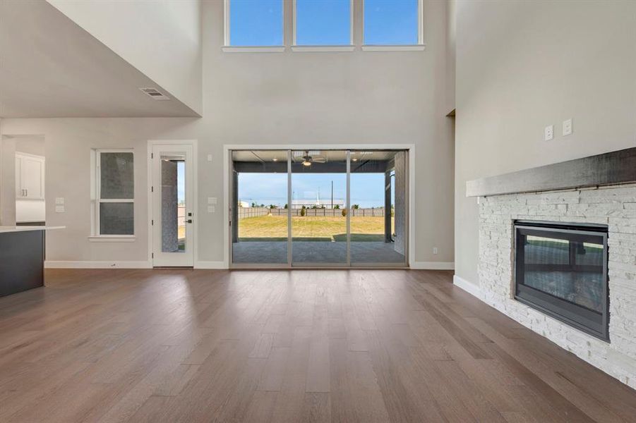 Unfurnished living room featuring a stone fireplace, dark wood-style flooring, and a high ceiling Unfurnished living room featuring a stone fireplace, dark wood-style flooring, and a high ceiling