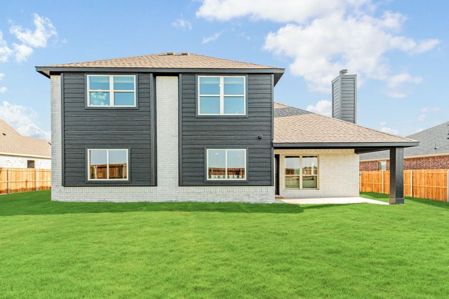 Two-story home rear view with dark gray siding, brick accents, covered patio, and fenced backyard lawn