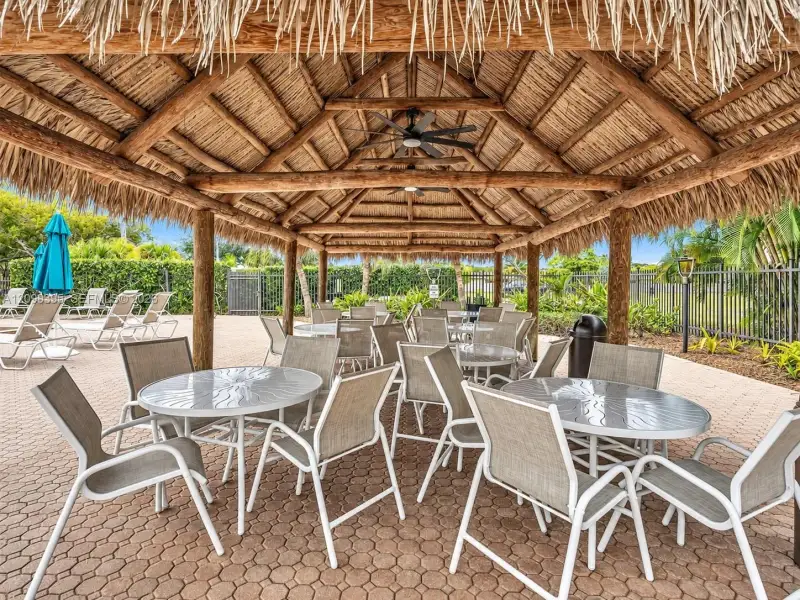 Outdoor pavilion featuring a thatched roof, exposed timber support beams, and ceiling-mounted fans over paved hardscaping