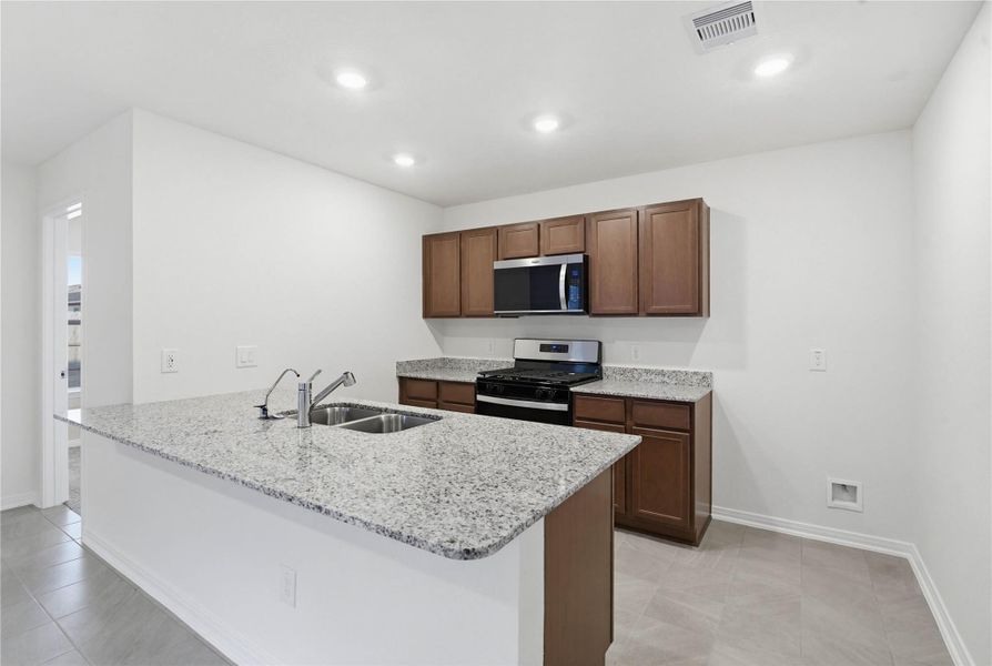 The kitchen exudes warmth with stunning Luna Pearl granite countertops perfectly paired with the rich, inviting tone of the Woodmont cabinetry in a Ginger stain. This combination creates a truly gorgeous and cohesive aesthetic.