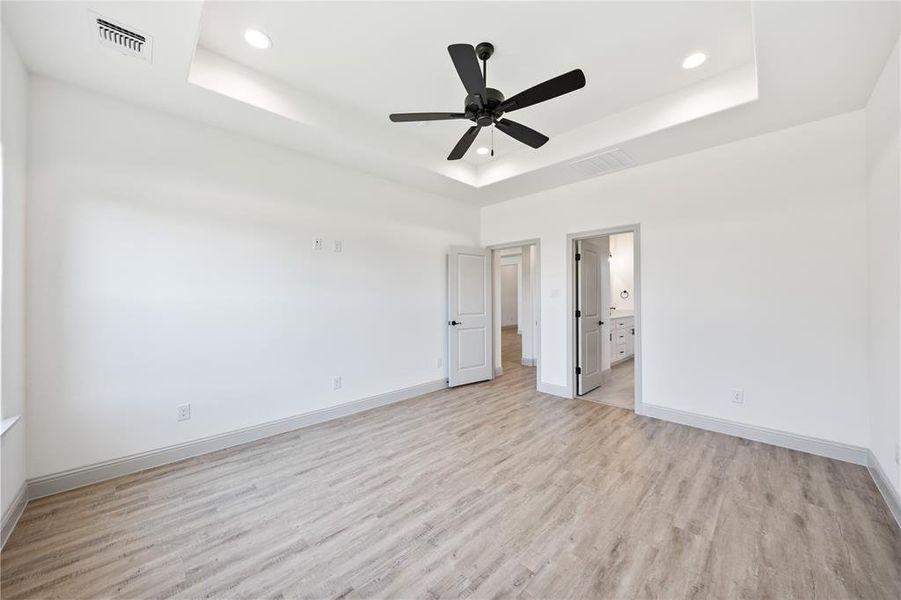 Unfurnished bedroom with a tray ceiling, light wood-type flooring, ceiling fan, connected bathroom, and recessed lighting
