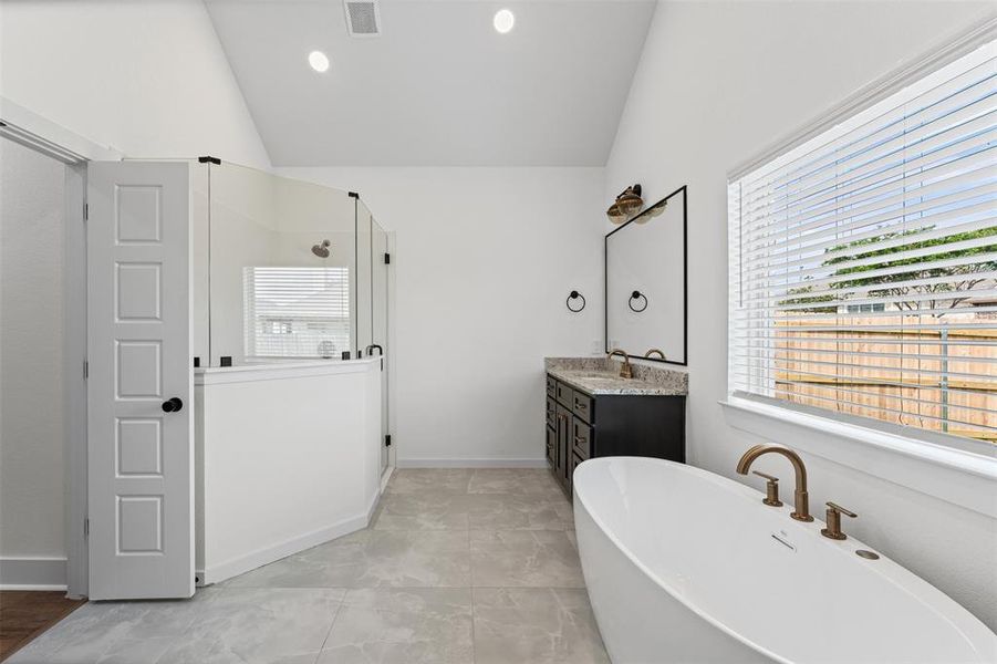 The bathroom features a freestanding tub with bronze fixtures, a double vanity with a dark cabinet and granite countertop, and a glass-enclosed shower