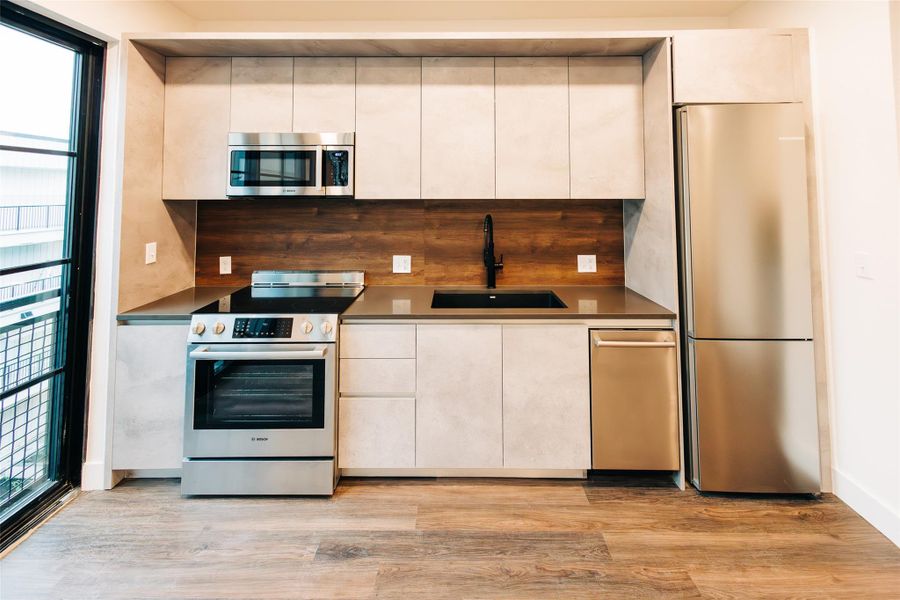 Kitchen with stainless steel appliances, tasteful backsplash, light wood-type flooring, dark countertops, and modern cabinets