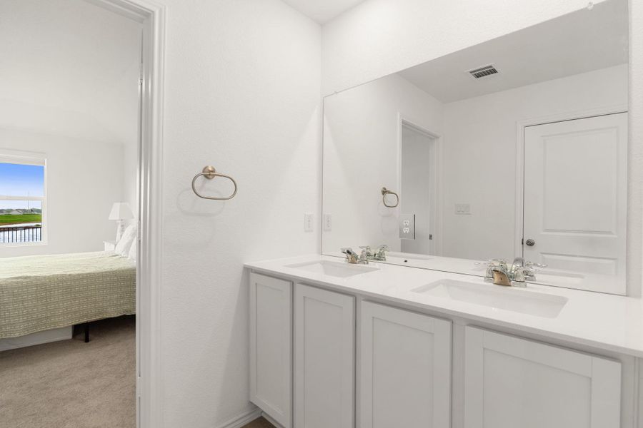 Double vanity in a bathroom with pristine white cabinetry and a view into a carpeted bedroom.