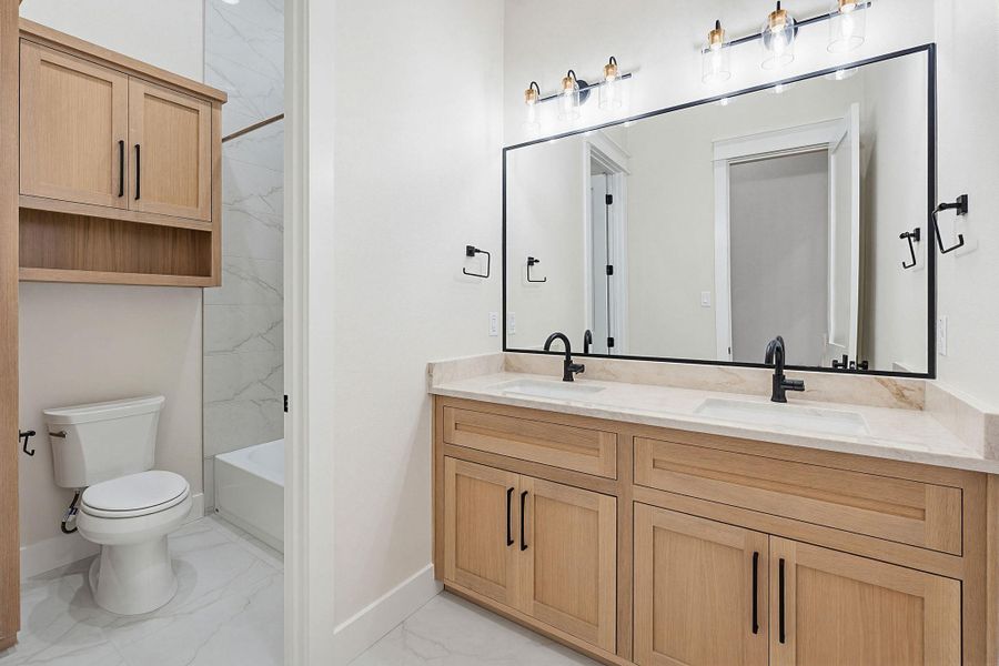 Bathroom featuring a dual vanity with light-tone wood-finish cabinetry, light-colored countertops, matte black fixtures, and an expansive framed mirror