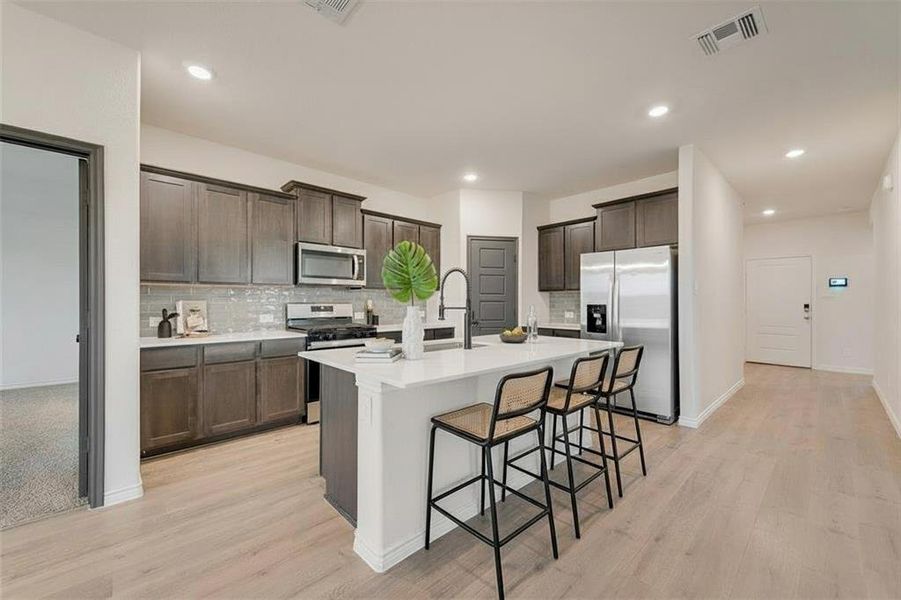 Kitchen featuring decorative backsplash, appliances with stainless steel finishes, a kitchen bar, dark brown cabinetry, and light wood-type flooring