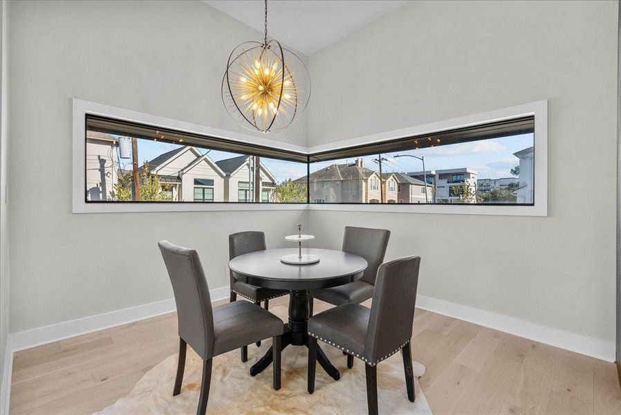 This photo showcases a modern dining nook with a round table and four chairs. The space features large corner windows with a view of neighboring houses, light wood flooring, and a stylish pendant light, creating a bright and inviting atmosphere. This photo showcases a modern dining nook with a round table and four chairs. The space features large corner windows with a view of neighboring houses, light wood flooring, and a stylish pendant light, creating a bright and inviting atmosphere.