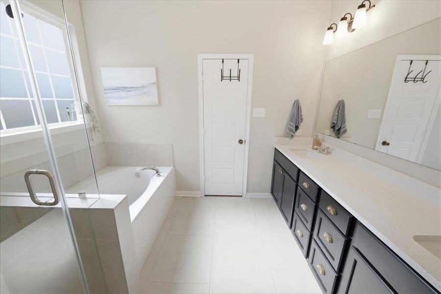 Primary, ensuite bath with double quartz vanity, a garden bath, a walk-in shower, and light tile patterned floors Primary, ensuite bath with double quartz vanity, a garden bath, a walk-in shower, and light tile patterned floors