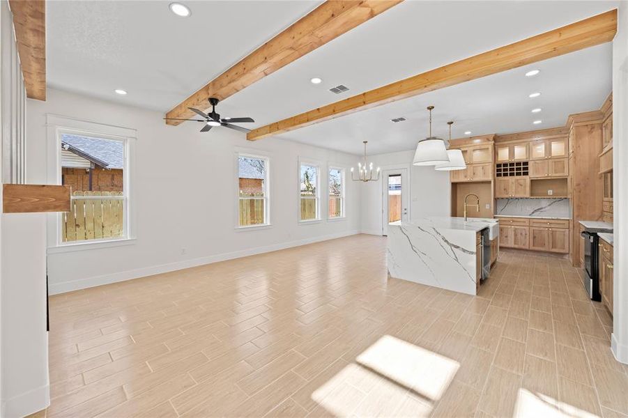 Kitchen featuring beamed ceiling, open floor plan, suspended lighting, decorative backsplash, and light stone countertops Kitchen featuring beamed ceiling, open floor plan, suspended lighting, decorative backsplash, and light stone countertops