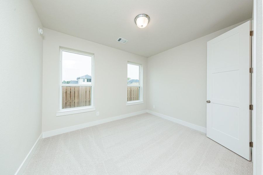 The ideal setup for multi-generational living or extended stays, this guest bedroom on the first floor includes its own dedicated en suite bath. It features high ceilings, large windows, plush carpet flooring, and neutral-toned walls.