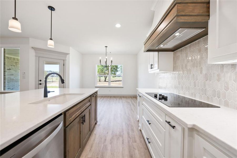 Kitchen with white cabinetry, hanging light fixtures, backsplash, stainless steel dishwasher, and light stone countertops