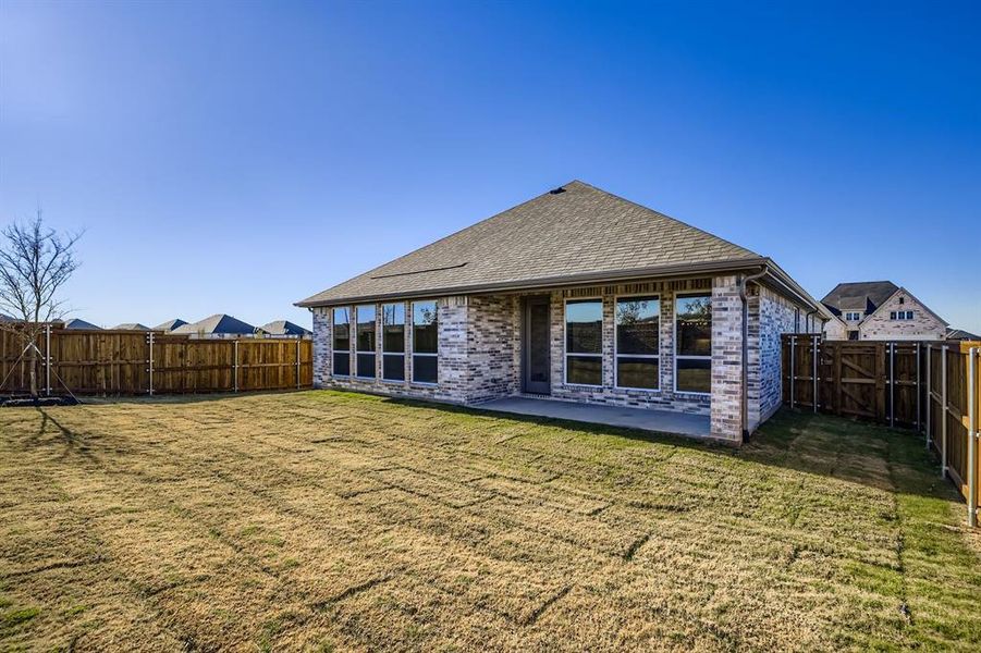 Rear view of house featuring brick siding, a patio, a fenced backyard, roof with shingles, and a gate