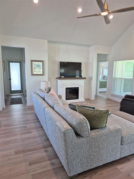 Living area featuring recessed lighting, light wood finished floors, a glass covered fireplace, a ceiling fan, and vaulted ceiling