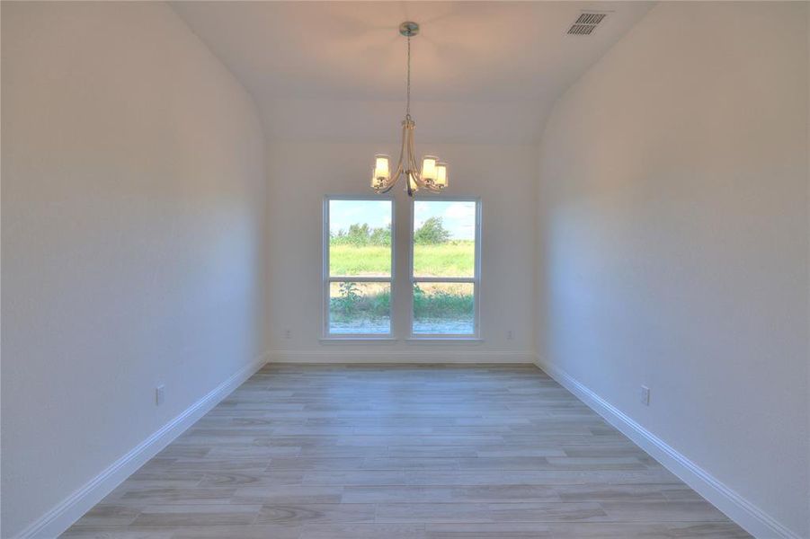 Spare room featuring a chandelier, vaulted ceiling, and light wood-style floors Spare room featuring a chandelier, vaulted ceiling, and light wood-style floors