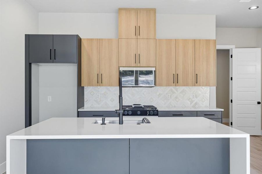 Kitchen with light stone counters, an island with sink, backsplash, modern cabinets, and light brown cabinets Kitchen with light stone counters, an island with sink, backsplash, modern cabinets, and light brown cabinets