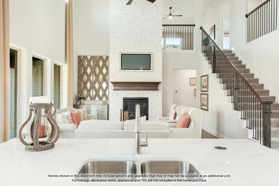 Open-concept living area with two-story stone fireplace, kitchen island sink, and staircase visible in background. Open-concept living area with two-story stone fireplace, kitchen island sink, and staircase visible in background.