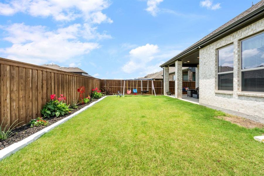 Spacious backyard featuring a manicured lawn, a full wooden privacy fence, and a stone-clad covered patio Spacious backyard featuring a manicured lawn, a full wooden privacy fence, and a stone-clad covered patio