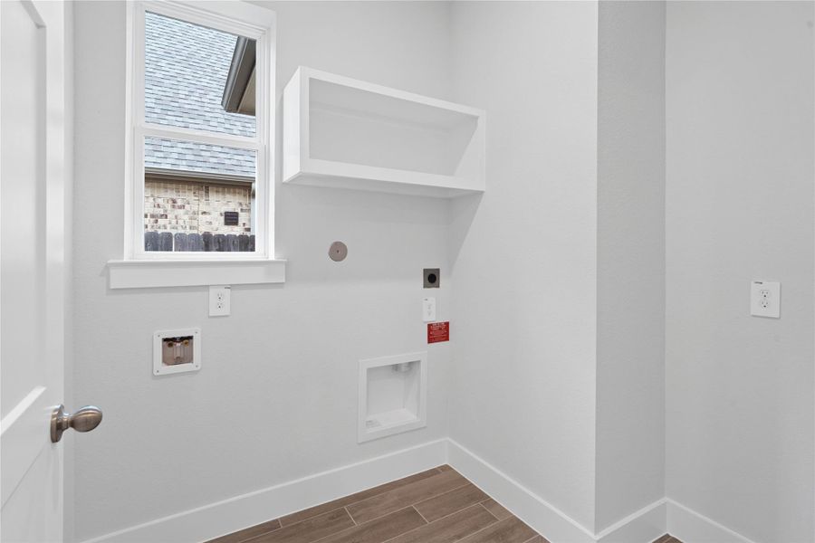 This bright and functional laundry room is conveniently located and ready for your appliances. It features clean white walls and trim, a large window providing abundant natural light, and the gorgeous wood tile flooring for durability.
