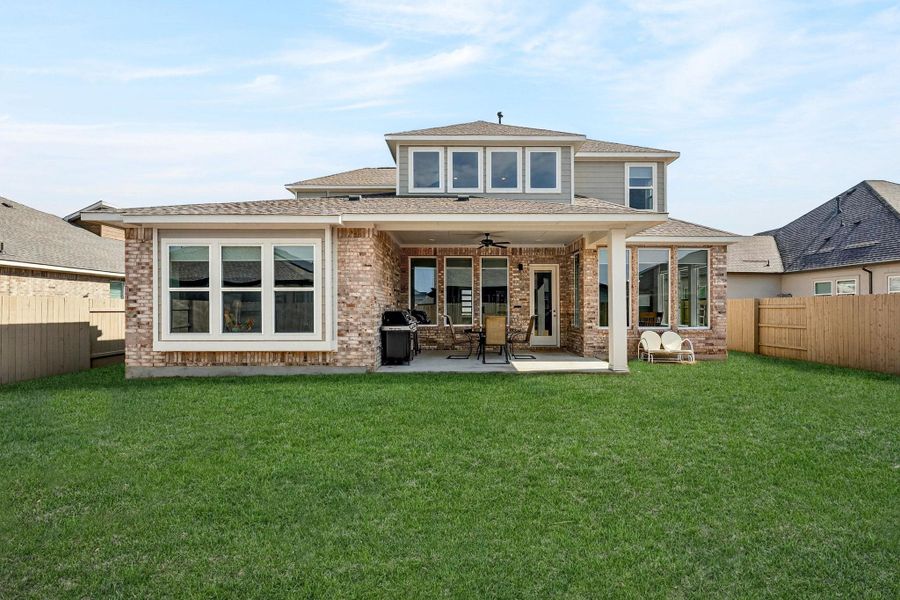 Rear view of the house featuring a fenced backyard, ceiling fan, brick siding, a patio, and a shingled roof