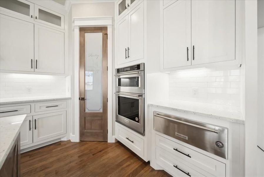 Kitchen featuring stainless steel double oven, dark hardwood / wood-style flooring, light stone countertops, and white cabinets