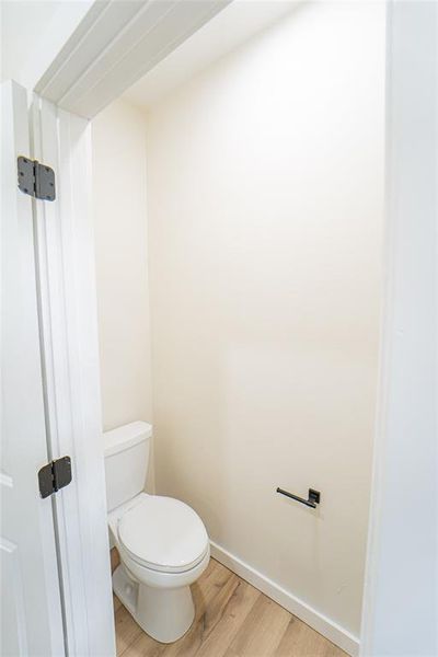 Powder room featuring a white toilet, wood-finish flooring, and a matte black toilet paper holder
