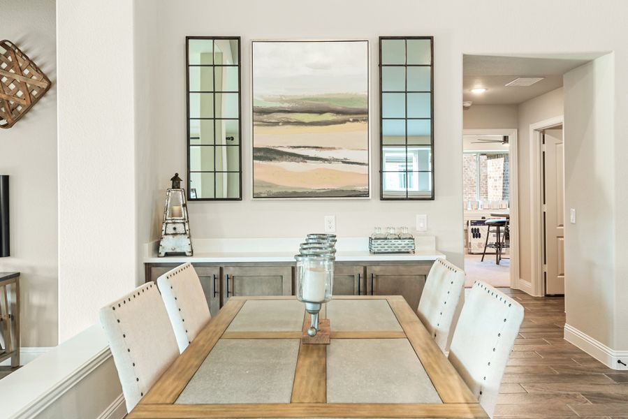 Dining room with wood table, white upholstered chairs, gray buffet, and framed wall art